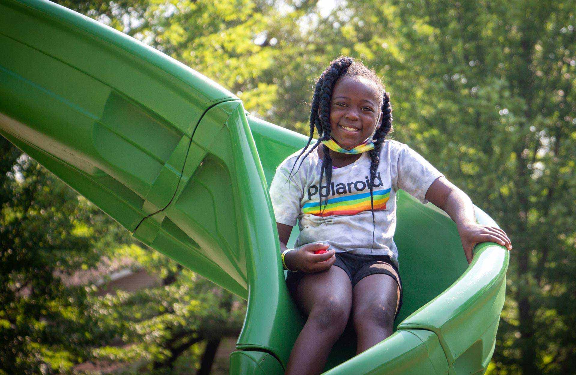African American young girl sliding down slide on playground
