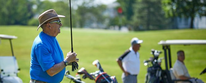 elderly white man carrying golf club on golf course