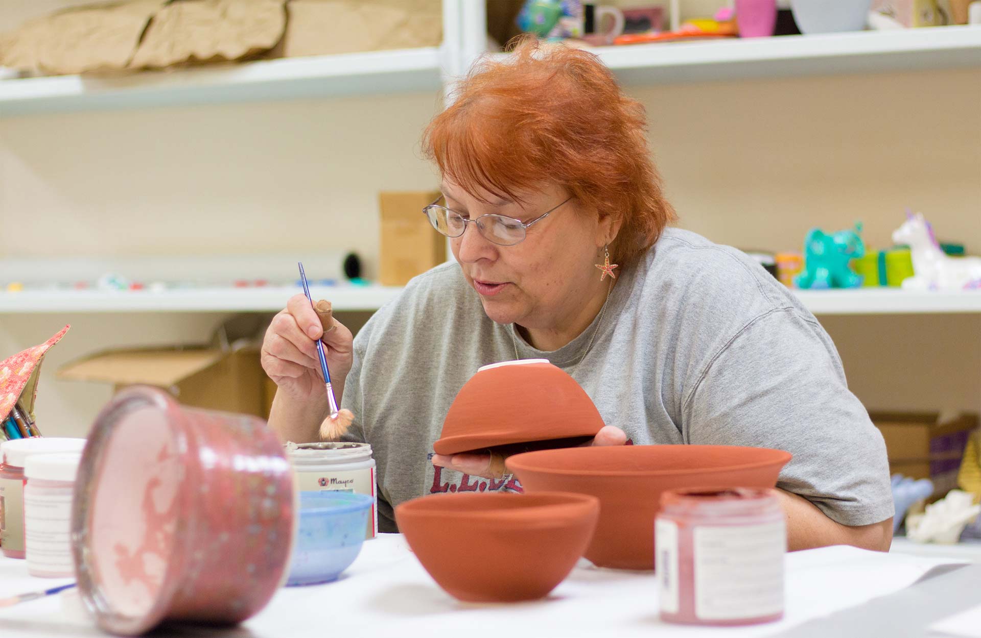 middle-aged white woman painting pottery in art program