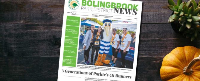 Bolingbrook Park District newsletter laying on top of desk. Photo of four women and Parkie the Pelican mascot after running Parkie's 5K.