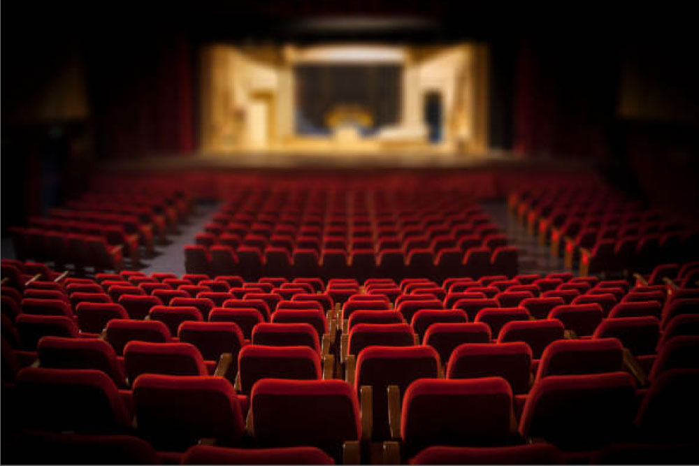An empty theater with red seats and a lit stage with props.