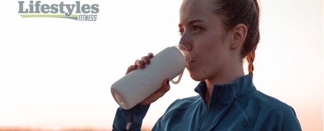 Caucasian women drinking from a water bottle with the Lifestyles Fitness text next to her