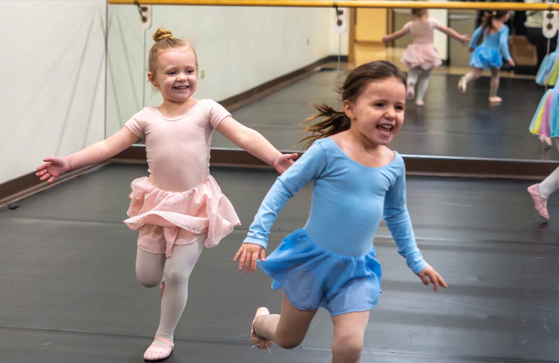 Two Caucasian toddlers in ballerina clothes dancing and laughing
