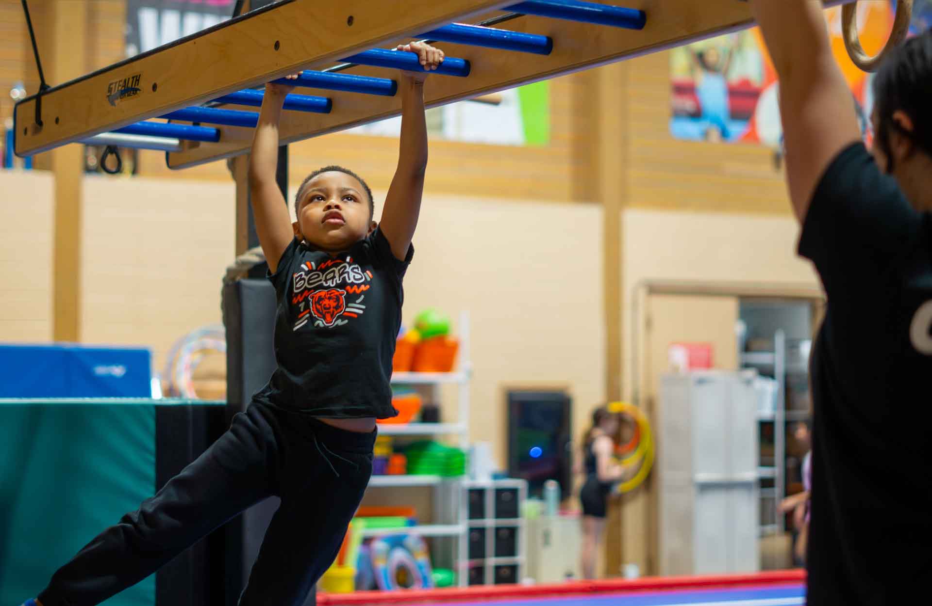 Young African-American boy hanging from bars in a Ninja class