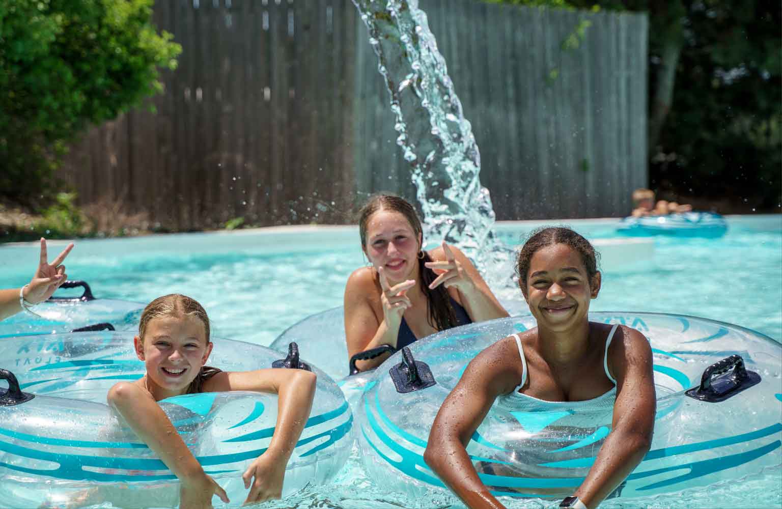 Two Caucasian girls and an African-American girl smiling and floating down the lazy river
